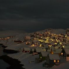 snow covered houses are lit up at night in the distance, with dark clouds overhead