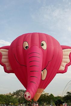 a large pink elephant balloon flying in the sky with people watching it from behind and onlookers