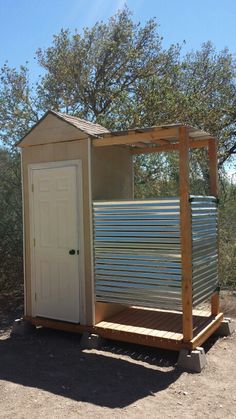 a small metal shed sitting in the middle of a dirt field next to a tree