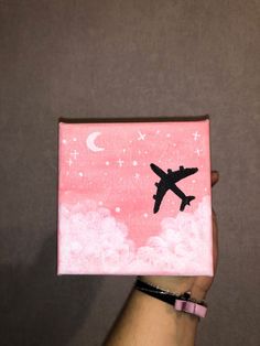 a hand holding up a small pink box with an airplane on the side and stars in the sky