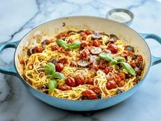 pasta with tomatoes and mushrooms in a blue skillet on a marble countertop next to a spoon