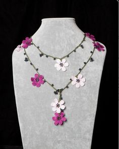 the necklace is decorated with pink and white flowers on a gray mannequin stand