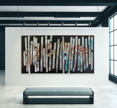 two paintings hanging on the wall next to a bench in an empty room with large windows