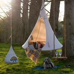 a dog laying in the grass next to a white hanging chair with pillows on it