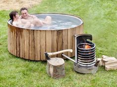 a man and woman sitting in an outdoor hot tub next to each other on the grass