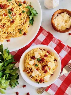 two white bowls filled with pasta and garnished with parsley on a red checkered tablecloth