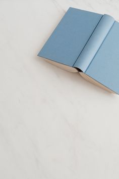 an open blue book sitting on top of a white table next to a cell phone