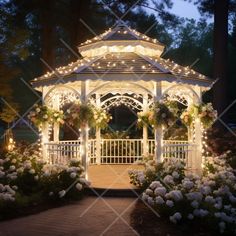 a white gazebo with lights and flowers around it at night in front of some trees