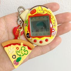 a hand holding a small gameboy keychain with a slice of pizza on it