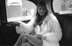 a woman sitting in the back seat of a car wearing a fur coat and jeans