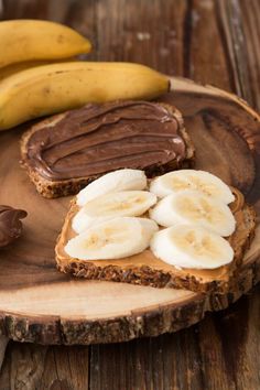 peanut butter and banana sandwich with chocolate spread on wooden plate next to two ripe bananas