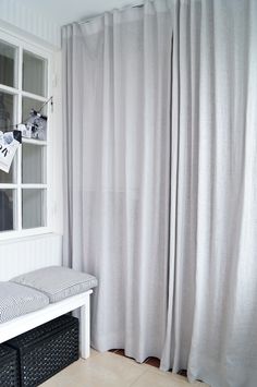 a white bench sitting in front of a window next to a gray and white curtain