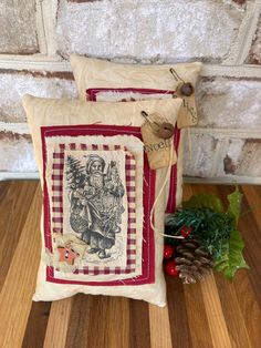 two decorative pillows sitting on top of a wooden floor next to a pine cone and holly