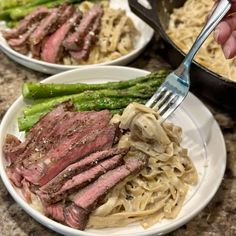 a plate with steak, noodles and asparagus is being held by a fork