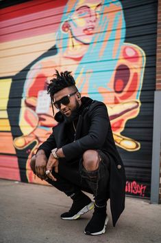 a man with dreadlocks squatting in front of a graffiti wall