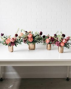 four gold vases with flowers on a white table