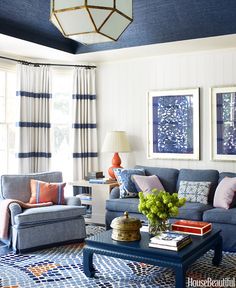 a living room filled with blue furniture and paintings on the wall above it's windows