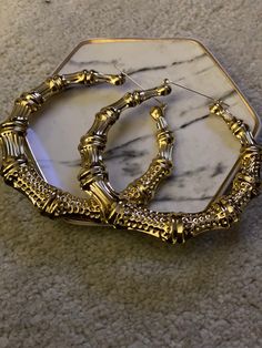 two gold bracelets sitting on top of a marble tray