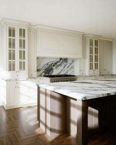 an empty kitchen with marble counter tops and white cabinetry, along with hardwood flooring