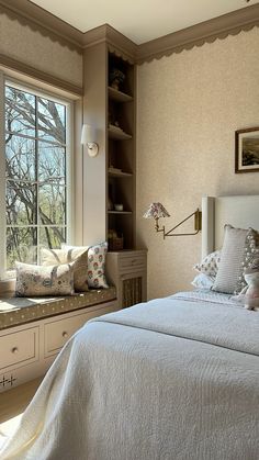 a bed sitting under a window next to a white dresser with drawers and pillows on top of it