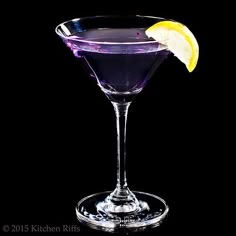 a purple drink with a lemon wedge on the rim in front of a black background