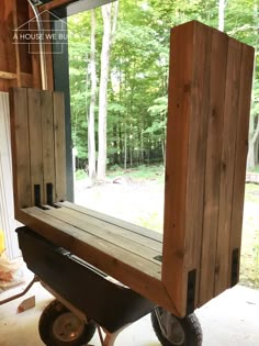 a wooden cart with wheels is sitting in front of a window that looks out onto the woods