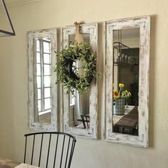 three mirrors hanging on the wall above a dining room table with a wreath and potted plant