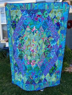 a woman holding up a blue and green quilt