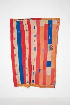 an orange, blue and red striped cloth hanging on a white wall next to a black cat