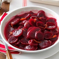 a white bowl filled with sliced beets on top of a table next to silverware