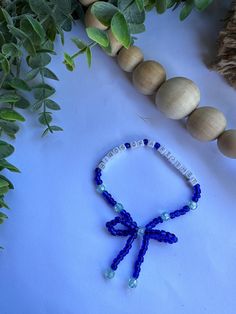 a beaded bracelet with blue beads and a bow on it next to some green leaves