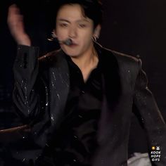 the man is wearing a black jacket and has his hands in the air as he sings