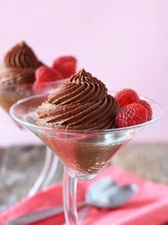 two desserts with chocolate frosting and raspberries in small glasses on a pink napkin