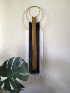 a wall hanging with two circular rings and three fringes on it next to a plant