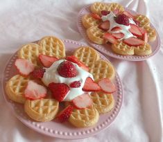 two waffles with strawberries and whipped cream on them are sitting on a pink plate