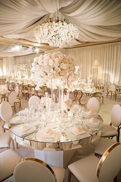 an elegant wedding reception with white flowers and chandeliers on the ceiling, all set up for a formal function