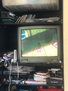 a television sitting on top of a wooden shelf filled with books and video game controllers