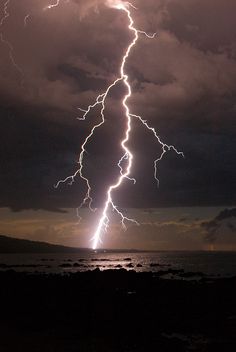 a lightning bolt hitting over the ocean at night