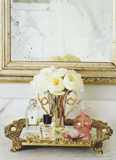 a gold tray with white flowers and perfume bottles on it in front of a mirror