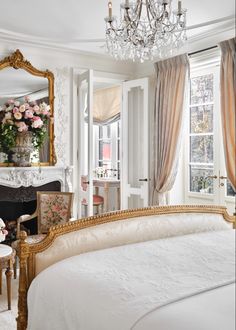 a white bed sitting in a bedroom next to a fire place and a chandelier