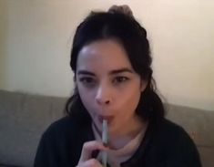 a woman holding a toothbrush in her mouth and looking at the camera while sitting on a couch