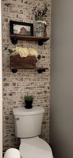 a white toilet sitting in a bathroom next to a wooden shelf with flowers on it