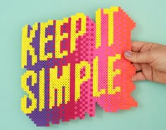 a hand holding up a piece of art made out of perforated paper that says keep it simple