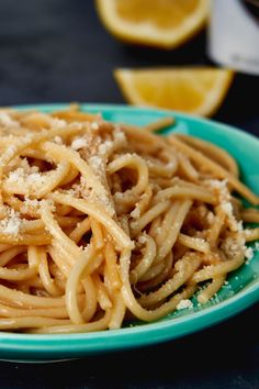 a plate of pasta with parmesan cheese and lemon wedges on the side