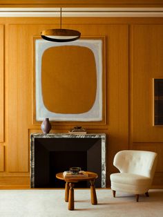 a chair and table in front of a fireplace with a painting on the wall behind it