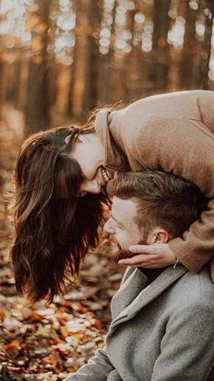 a man and woman are kissing in the woods with leaves on the ground behind them