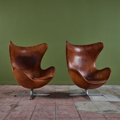 two brown leather chairs sitting on top of a tiled floor