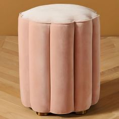 a pink velvet stool with brass legs on a wooden floor in front of a beige wall