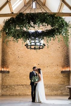 a bride and groom standing in front of a chandelier with greenery hanging from it