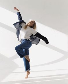 a woman in jeans and a white shirt is doing a dance move with her arms outstretched